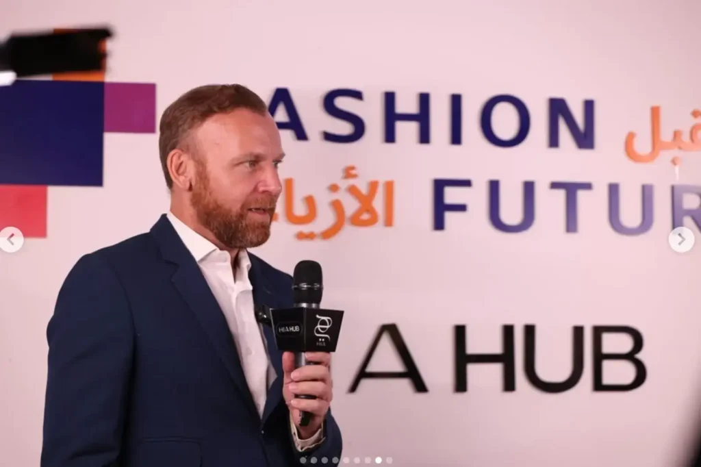 Burak Cakmak-en costume et chemise blanche avec un micro pour présenter fashion Week Ryad